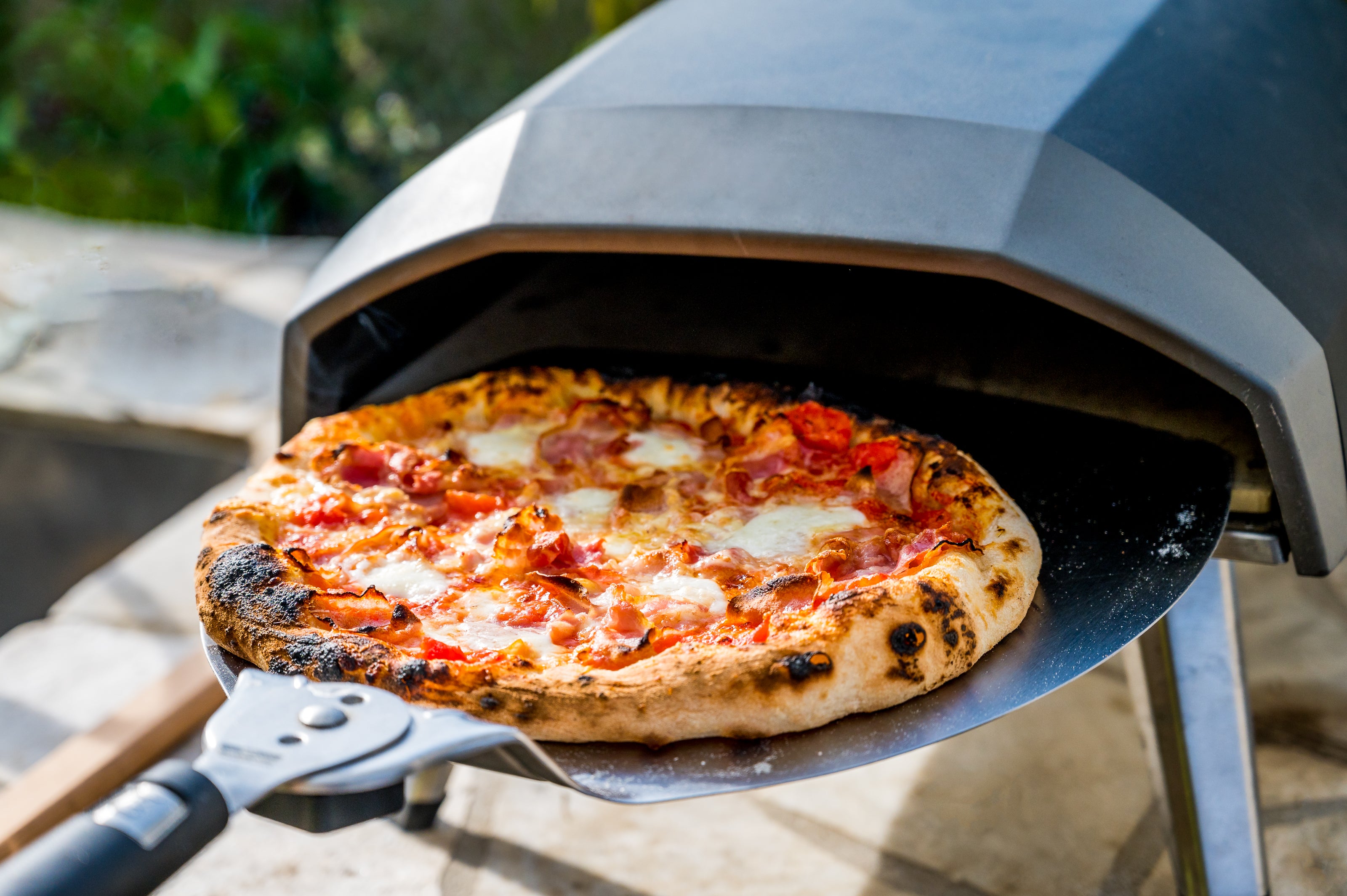 a meat lover pizza going into a summer oven with a warm flame.